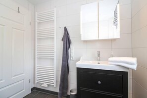 A modern bathroom with a white door, a towel rack with a towel, a white sink with a mirror above it, and a black cabinet below.