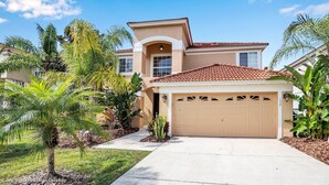 A two-story house with a beige facade, a red-tiled roof, and a garage. - Spacious Pool Area With Lake View - 5bd/4.5ba Pool Home #5av139 (Davenport)