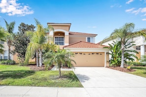 A two-story house with a tiled roof, a garage, and a well-maintained lawn with palm trees. - Spacious Pool Area With Lake View - 5bd/4.5ba Pool Home #5av139 (Davenport)