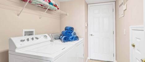 Un cuarto de lavado con lavadora y secadora apiladas, un estante con toallas dobladas y una puerta con un cartel.