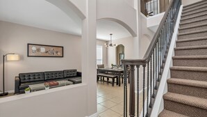 A spacious living room with a black leather sofa, a glass coffee table, and a dining area with a chandelier. - Spacious Pool Area With Lake View - 5bd/4.5ba Pool Home #5av139 (Davenport)