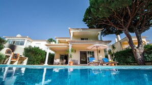 A poolside area with a clear blue pool, lounge chairs, and a large tree. - Villa Luz - Stunning 4-Bed Villa (Vilamoura)