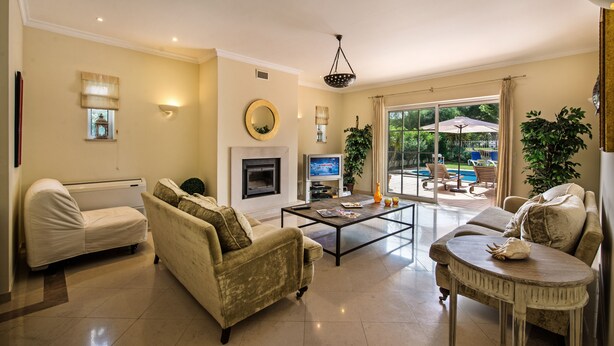 A living room with a fireplace, sofas, a coffee table, and a view of an outdoor pool area. - Villa Luz - Stunning 4-Bed Villa (Vilamoura)