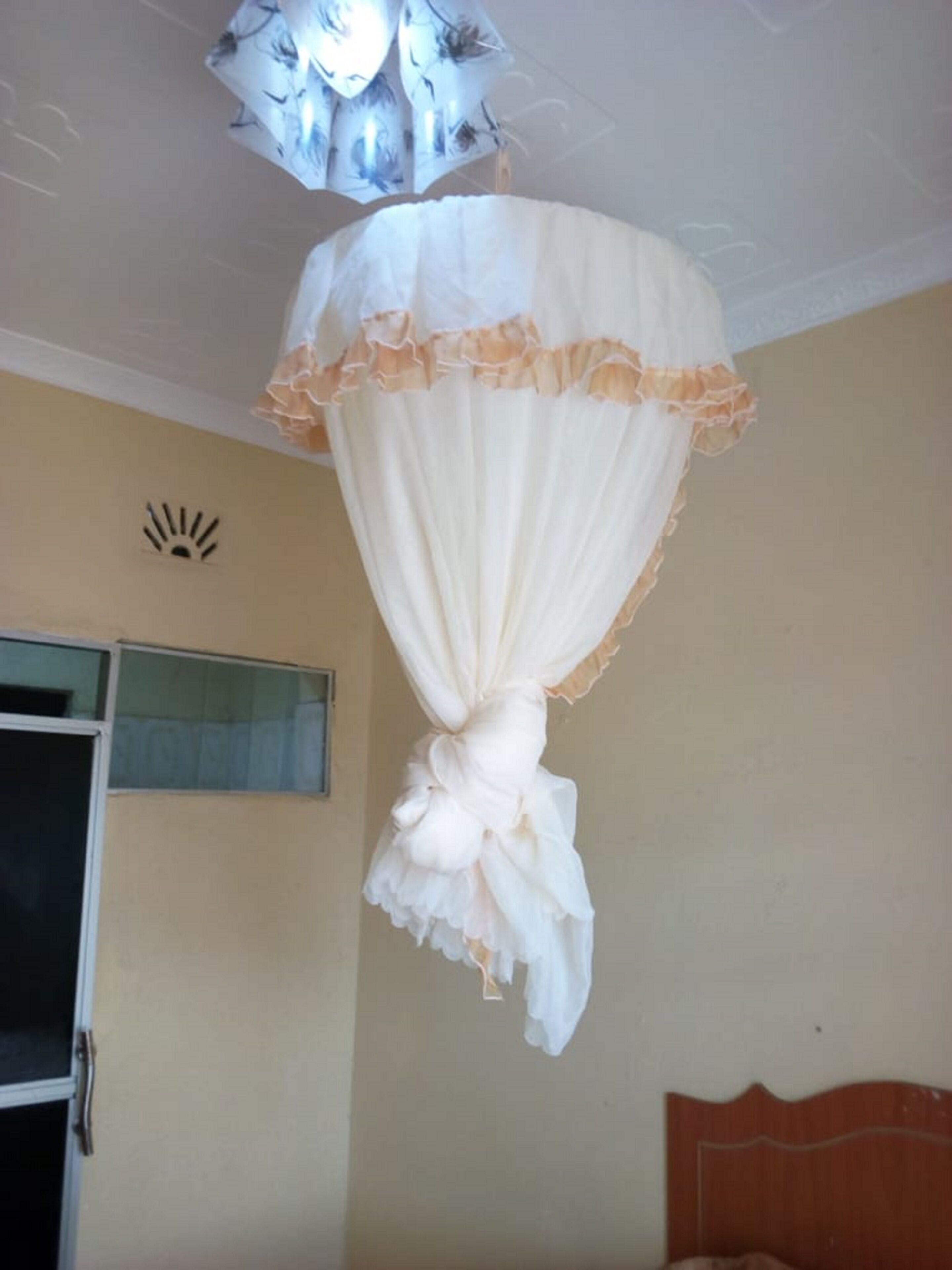 A room with a bed, a window with a curtain, and a ceiling light fixture.