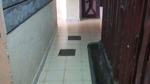 A narrow hallway with tiled flooring, a wooden door with a decorative design, and a wall with a textured pattern. - Silver Spoon Motel (Kerugoya)