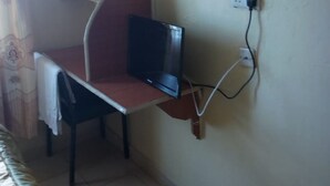 A compact room with a bed, a desk with a chair, and a wall-mounted TV. - Silver Spoon Motel (Kerugoya)