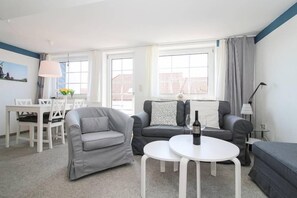 Un salon moderne avec un canapé gris, une table basse blanche et un coin repas comprenant des chaises et une table blanches.