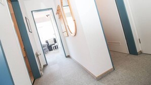 Un couloir avec une porte donnant sur une pièce, un miroir en bois accroché au mur et un tableau encadré.