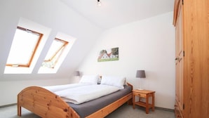 Une chambre à coucher avec un lit en bois, deux tables de chevet, une armoire et des fenêtres de toit.