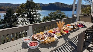 Una larga mesa con diversos platos y aperitivos en un balcón con vista a un lago.