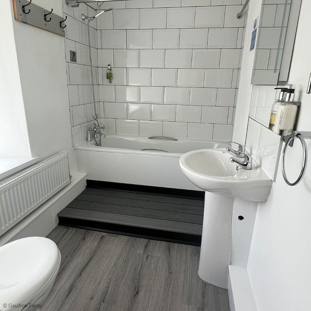 A modern bathroom with a white bathtub, a white sink, and a toilet. There is a towel rack above the sink and a mirror on the wall.