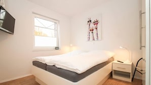 A bedroom with a bed, a bedside table, a lamp, a TV, and a window. - Leystuuv (Krummhoern)