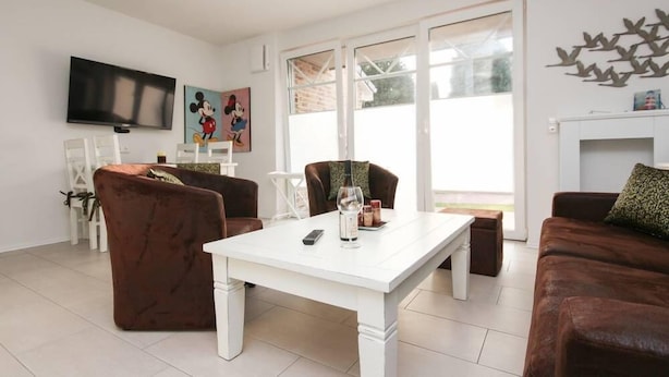 A living room with a white table, brown sofas, a TV, and a painting of Mickey Mouse. - Leystuuv (Krummhoern)