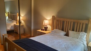 Ein Hotelzimmer mit einem hölzernen Bett, einem Nachttisch mit Lampe, einem Spiegel und einem Beistelltisch.