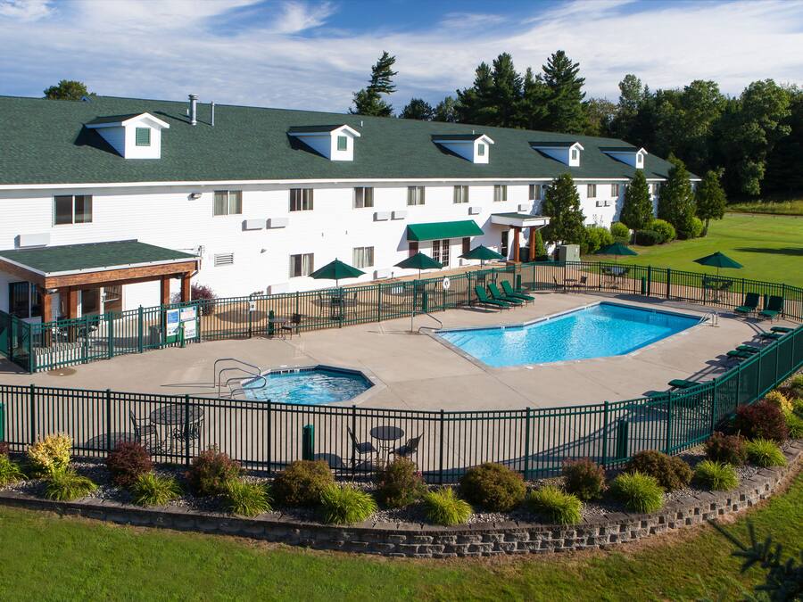 A large hotel with a swimming pool, outdoor seating, and a well-maintained lawn.