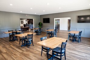 A spacious room with multiple wooden tables and chairs, a television mounted on the wall, and a plant in the corner. - Manistee National Golf and Resort (Manistee)