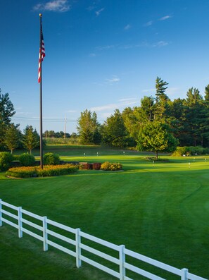 A golf course with a flagpole, trees, and a white fence. - Manistee National Golf and Resort (Manistee)