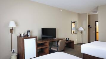 Ein Hotelzimmer mit einem Bett, einem Schreibtisch mit Fernseher, einem Sessel und zwei Lampen.