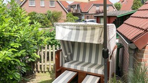 En randig loungestol för utomhusbruk med ett solskydd, ett trästaket och ett hus i tegel som syns i bakgrunden.