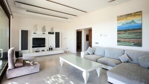 A modern living room with a flat-screen TV, a large painting, and a grey sofa.