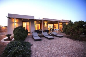 A modern building with a covered outdoor seating area, a stone wall, and a gravel driveway.
