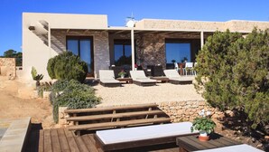 A modern villa with a wooden deck, outdoor seating, and a stone wall.