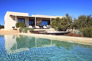 A modern building with a pool, outdoor seating, and a stone facade. - Romero en Can Corda, Chalet 4 Dormitorios 4 Baños con piscina en Cap de Barbaria Formentera (Sant Francesc de Formentera)