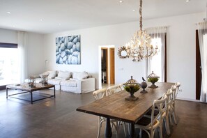 Cozy living area with a large dining table for six, a stylish chandelier, and a beautiful abstract painting.