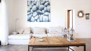 A modern living room with a white sofa, a wooden coffee table, and a large abstract painting on the wall. - Santolina en Can Corda, Chalet 4 Dormitorios 3 Baños con piscina en Cap de Barbaria Formentera (Sant Francesc de Formentera)