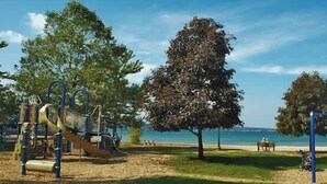 Un parque infantil con toboganes y estructuras para escalar, una banca y un árbol grande.