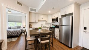 Una cocina moderna con armarios blancos, electrodomésticos de acero inoxidable y un comedor con mesa y sillas de madera.