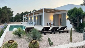 Area piscina moderna all'aperto con lettini, una zona relax coperta e un giardino di cactus.