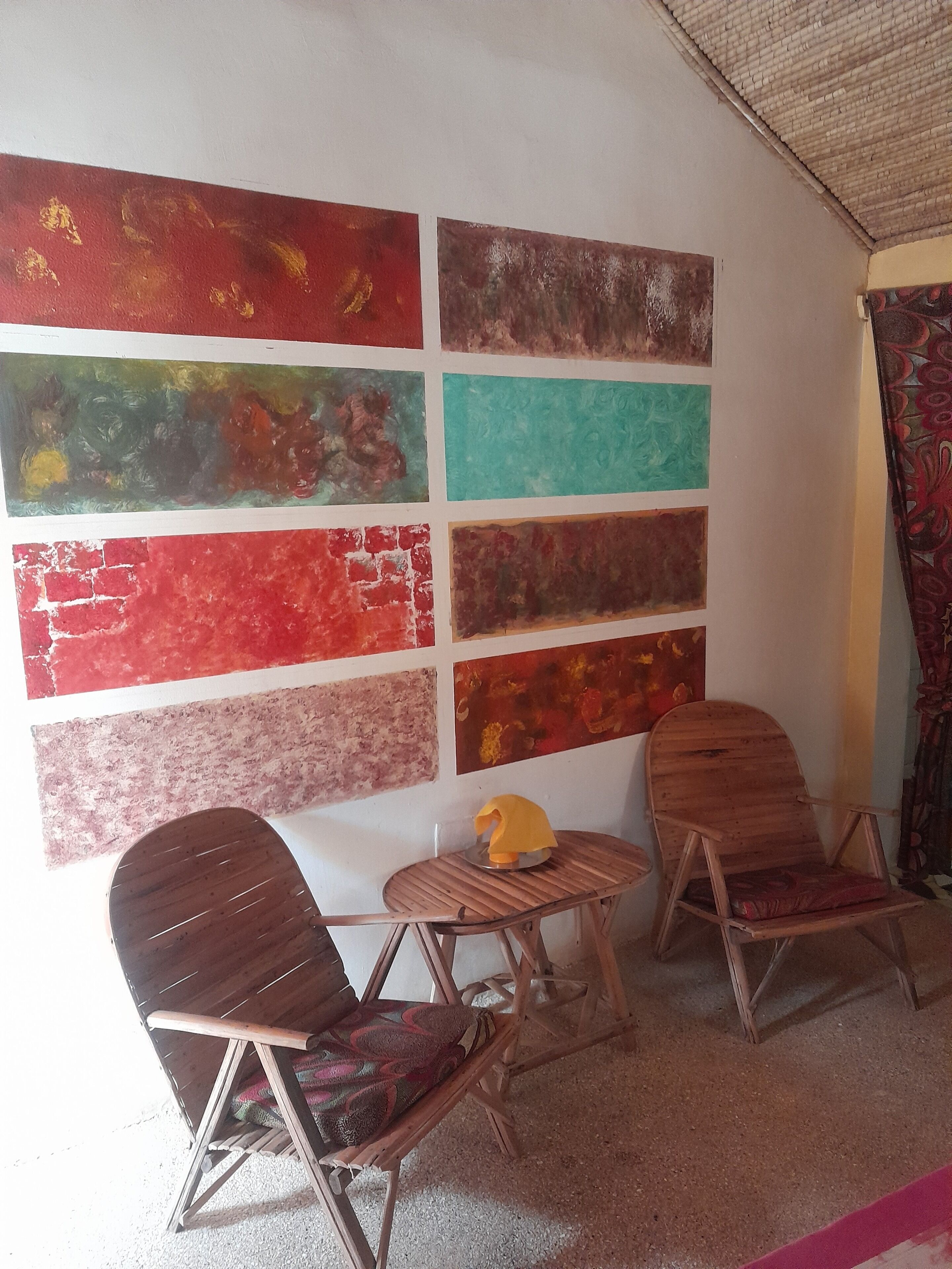 A room with a wall adorned with large abstract paintings, two wooden chairs, and a small wooden table.