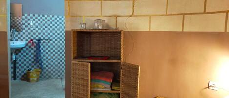 A small, compact room with a checkered floor, a brick wall, a wicker shelf with items, and a small stool.