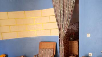A room with a blue wall, a wooden chair, a bed, a wicker basket, and a small table with a lamp.