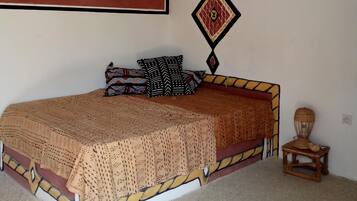 Een kamer met een bed, een muur met geometrische kunst, een decoratief kussen en een kleine tafel met een lamp.