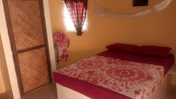 A room with a bed, a window with curtains, a wall-mounted artwork, and a door with a woven screen.