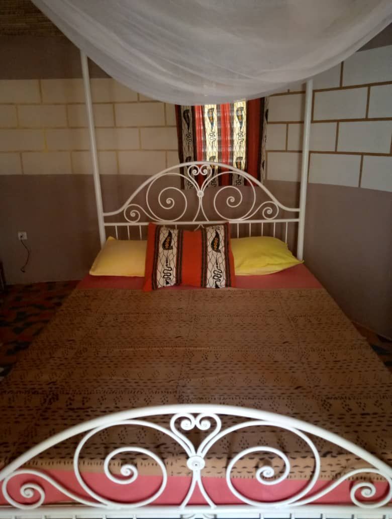 A single bed with a white metal frame, a patterned bedspread, and two pillows.
