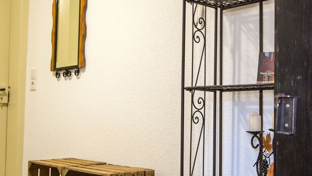 Un pasillo con un banco de madera, una estantería metálica y un espejo en la pared.