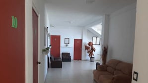 Un pasillo con una puerta roja identificada con el número 10, un sofá marrón y una planta en maceta.