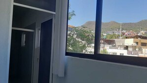 Una habitación con ventana que da a un paisaje urbano y colinas.