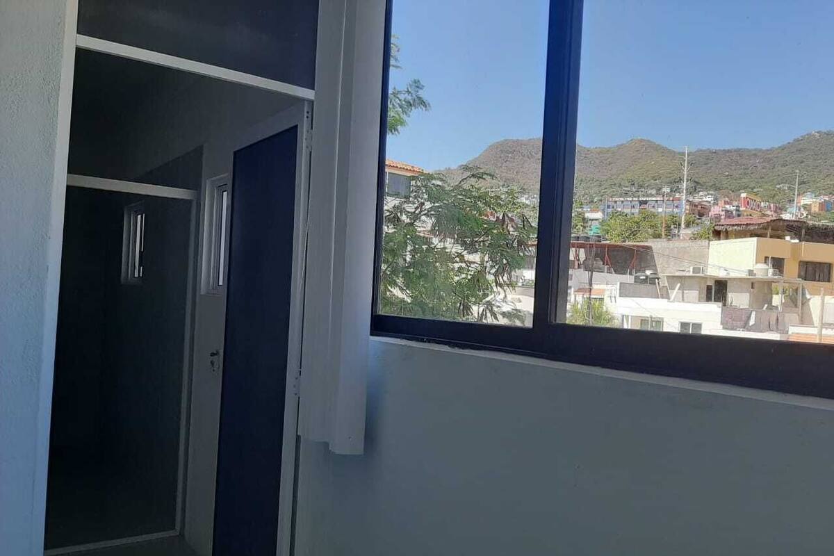 A room with a window overlooking a cityscape and hills.