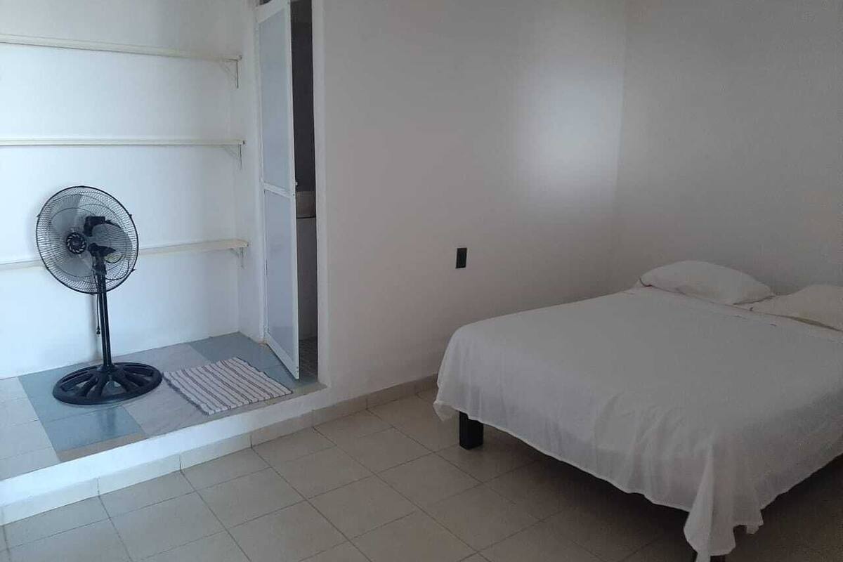 A bedroom with a bed, a standing fan, and a door leading to a balcony.