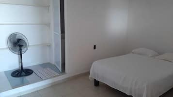 A bedroom with a bed, a standing fan, and a door leading to a balcony.