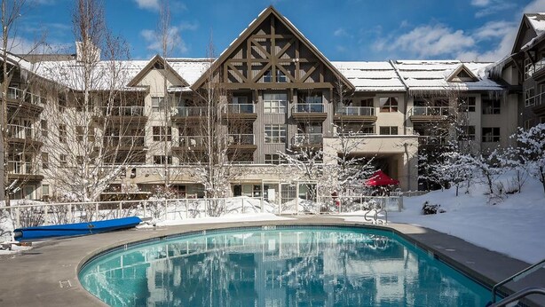 A hotel with a pool, snow-covered trees, and a clear blue sky. - Luxury Ski-in/out 1Br/1Ba - 3Hot Tub`s & Pool (Whistler)