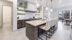 A modern kitchen with a central island, pendant lighting, and a dining area with bar stools.