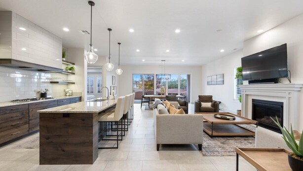A modern kitchen with a central island, dining area with chairs, a sofa, and a fireplace.