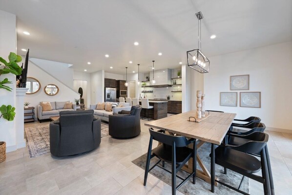 A spacious living area with a dining table, sofas, and a staircase leading to another level.