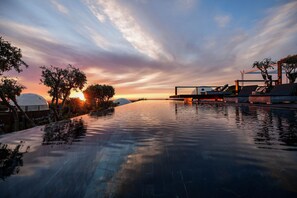 An infinity pool with a sunset view, lounge chairs, and a pergola structure. - wecamp Reserva Alecrim (Santiago do Cacém)