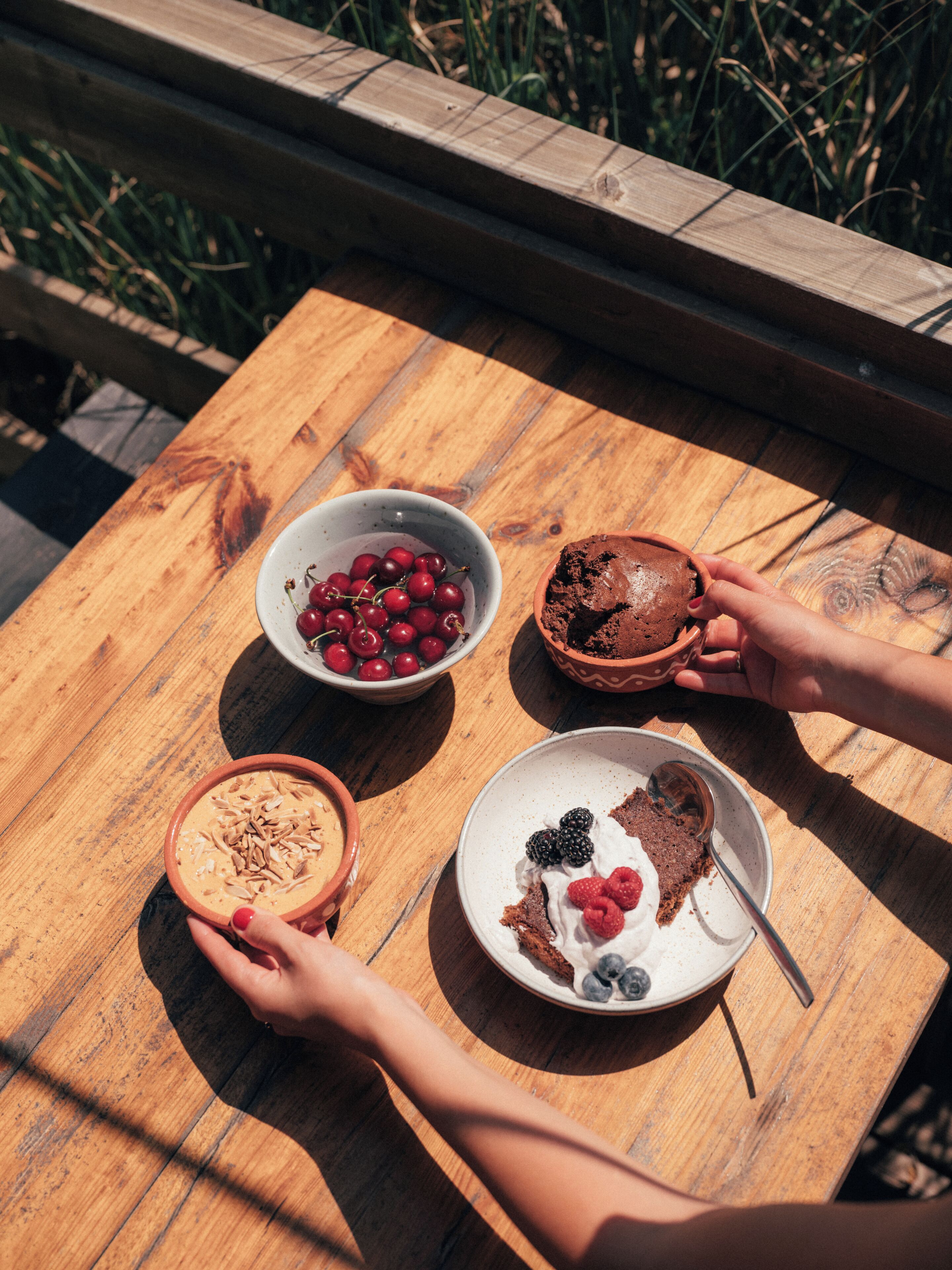 Un tavolo di legno con tre ciotole di cibo: una con ciliegie, una con torta al cioccolato e una con frutti di bosco e panna.